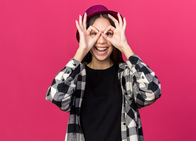 Sorridente giovane bella ragazza che indossa un cappello da festa che mostra gesto di sguardo