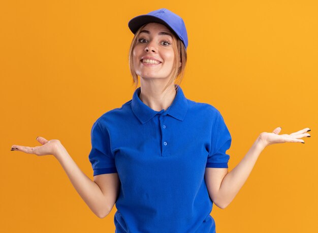 Sorridente giovane bella ragazza di consegna in uniforme che tengono le mani aperte sull'arancio