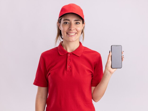 Sorridente giovane bella ragazza di consegna in uniforme tenendo il telefono su bianco