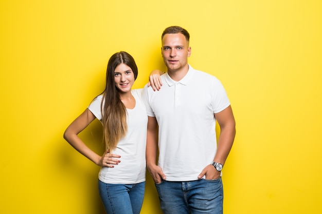 Sorridente giovane coppia isolata su sfondo giallo che abbracciano insieme vestiti in magliette bianche