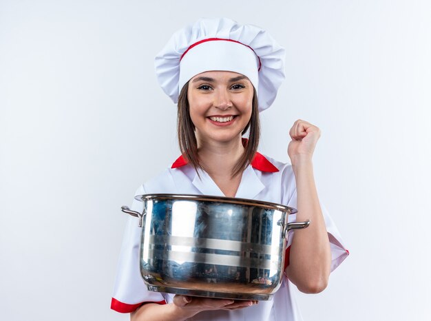 Sorridente giovane cuoca che indossa l'uniforme dello chef che tiene in mano una pentola che mostra sì gesto isolato su sfondo bianco