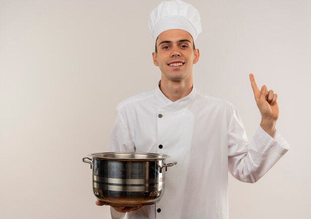 Sorridente giovane cuoco maschio indossa uniforme chef azienda pentola punta il dito verso l'alto con lo spazio della copia