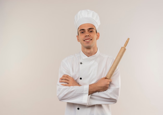 Sorridente giovane cuoco maschio indossa uniforme chef incrocio mani tenendo il mattarello con copia spazio