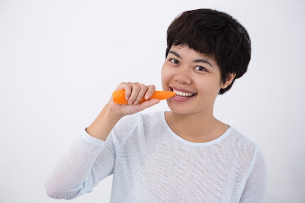 Sorridente giovane donna asiatica che morde la carota