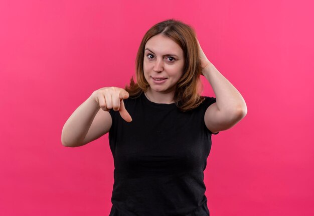 Sorridente giovane donna casual che punta con la mano dietro la testa su uno spazio rosa isolato