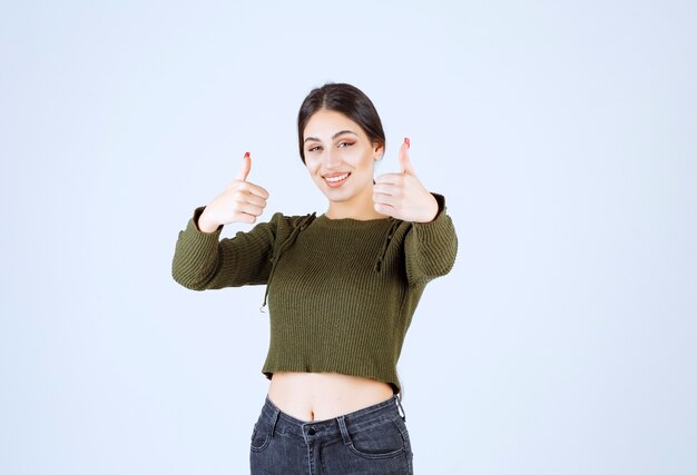 Sorridente giovane donna che dà i pollici in su su sfondo bianco.