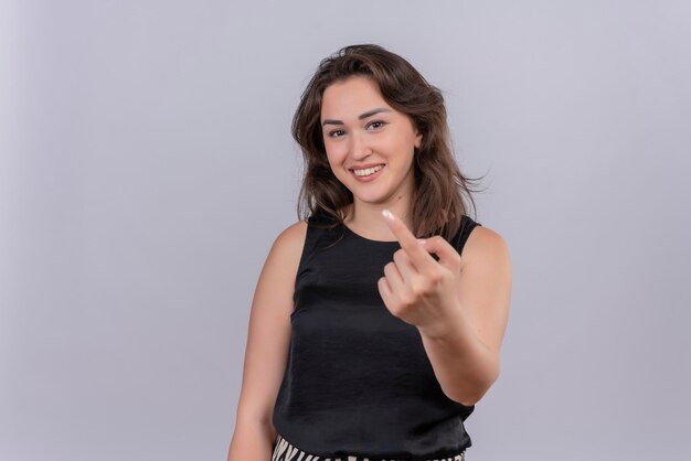 Sorridente giovane donna che indossa maglietta nera che mostra vieni sul gesto sulla parete bianca