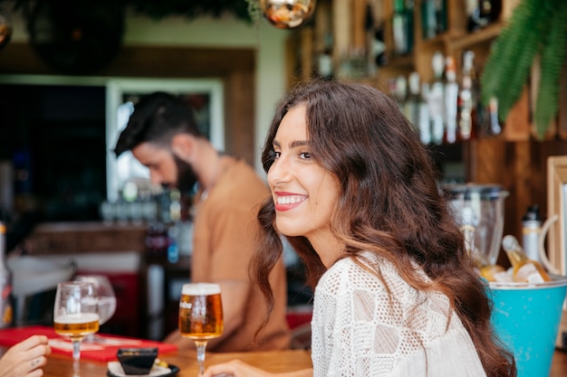 Sorridente giovane donna con birra al bar