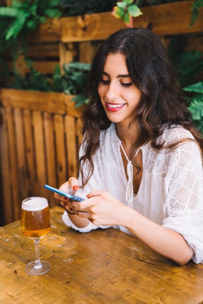 Sorridente giovane donna con smartphone e birra