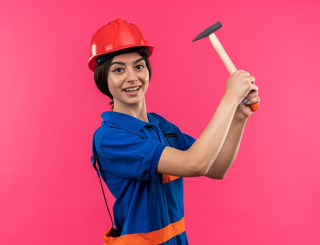 Sorridente giovane donna costruttore in uniforme alzando martello