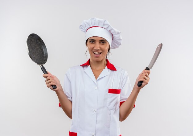 Sorridente giovane donna cuoco che indossa uniforme da chef tenendo padella e mannaia con copia spazio