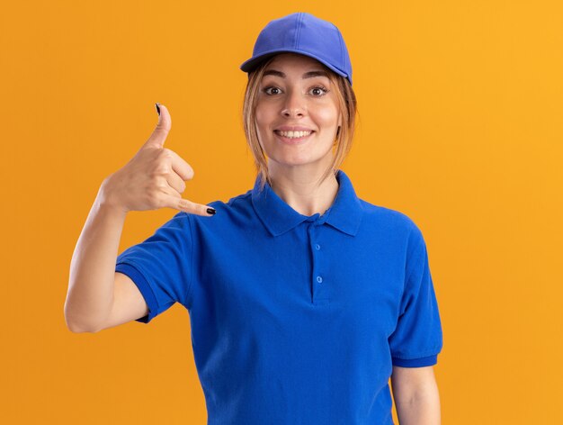 Sorridente giovane donna graziosa di consegna in uniforme facendo appendere sciolto gesto isolato sulla parete arancione