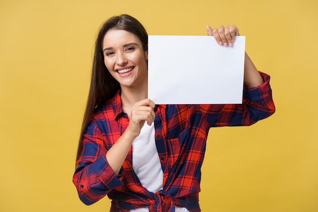 Sorridente giovane donna in possesso di foglio di carta bianca. Ritratto in studio su sfondo giallo.