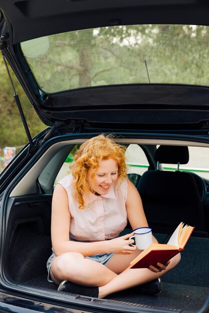 Sorridente giovane donna lettura libro in viaggio