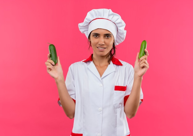 Sorridente giovane femmina cuoco indossando chef uniforme tenendo il cetriolo con copia spazio