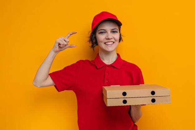 Sorridente giovane graziosa donna delle consegne che tiene in mano scatole per pizza e finge di tenere qualcosa