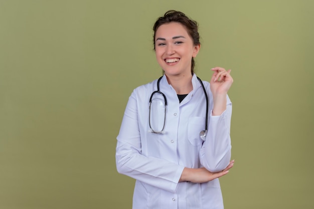 Sorridente giovane medico indossando abito medico indossando stetoscopio sulla parete verde