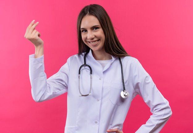 Sorridente giovane medico ragazza indossa stetoscopio camice medico che mostra il gesto di punta su sfondo rosa isolato