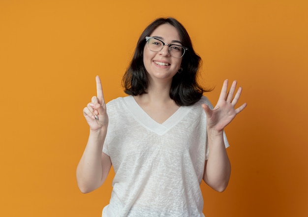 Sorridente giovane ragazza abbastanza caucasica con gli occhiali che mostra sei con le mani isolate su sfondo arancione con copia spazio