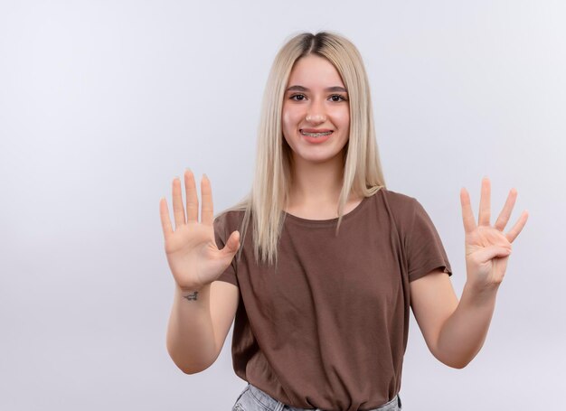 Sorridente giovane ragazza bionda in parentesi graffe dentale che mostra cinque e quattro su uno spazio bianco isolato con spazio di copia