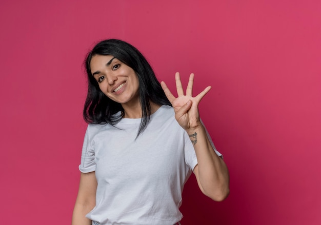 Sorridente giovane ragazza bruna caucasica gesti quattro con la mano isolata sulla parete rosa