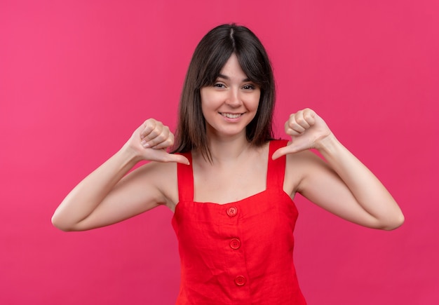 Sorridente giovane ragazza caucasica si punta con entrambe le mani su sfondo rosa isolato