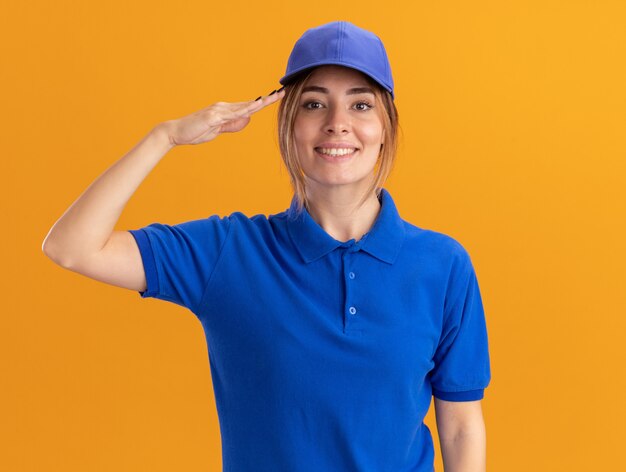 Sorridente giovane ragazza graziosa di consegna in uniforme che fa gesto di saluto sull'arancio