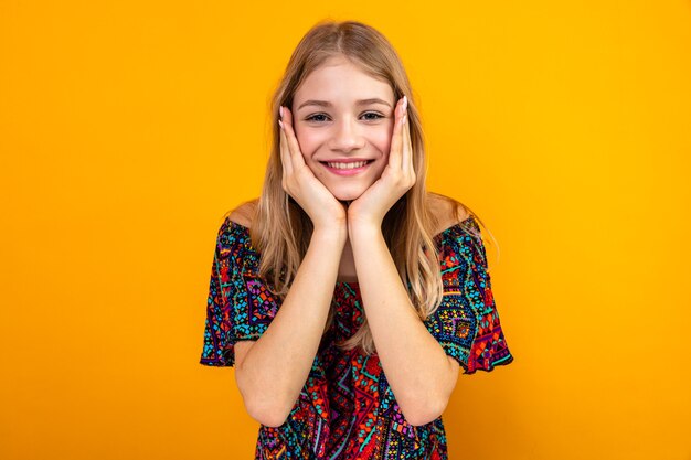 Sorridente giovane ragazza slava bionda che si mette le mani sul viso e guarda davanti