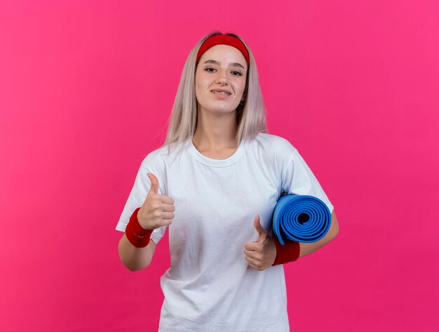 Sorridente giovane ragazza sportiva caucasica con le parentesi graffe che indossa la fascia