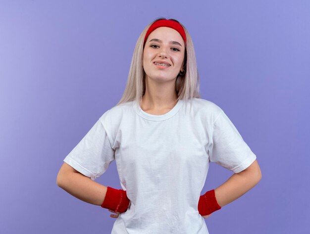 Sorridente giovane ragazza sportiva caucasica con le parentesi graffe che indossa la fascia