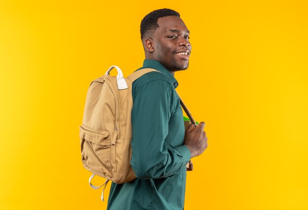 Sorridente giovane studente afroamericano con zaino in piedi, vista laterale