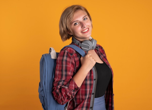 Sorridente giovane studentessa slava con le cuffie che indossa lo zaino si erge lateralmente