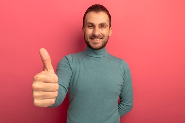 Sorridente giovane uomo caucasico che mostra il pollice in alto isolato sulla parete cremisi con lo spazio della copia