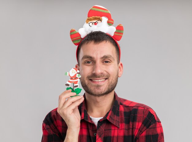Sorridente giovane uomo caucasico indossando la fascia di Babbo Natale tenendo il pupazzo di neve giocattolo di Natale guardando la telecamera isolata su sfondo bianco