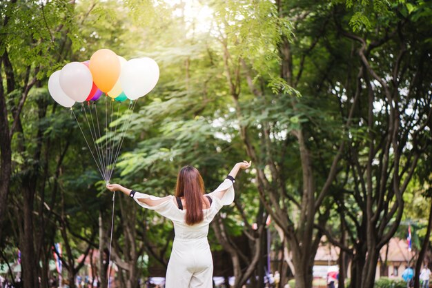 Sorridente giovani belle donne asiatiche con lunghi capelli castani nel parco. Con palloncini d&#39;aria color arcobaleno nelle sue mani.sunny e energia positiva della natura.