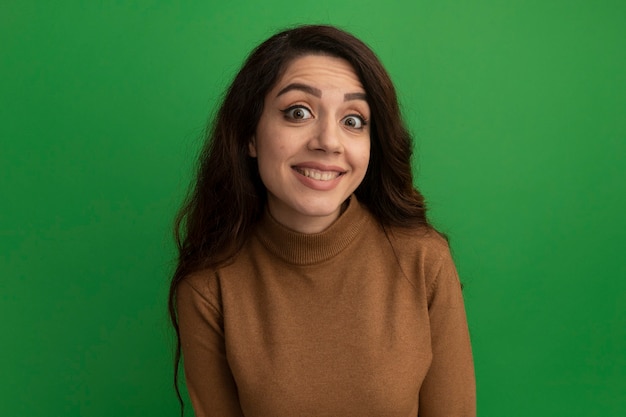 Sorridente guardando davanti giovane bella ragazza isolata sulla parete verde