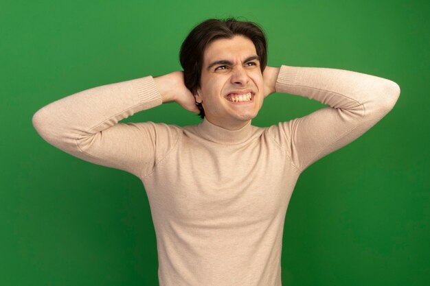 Sorridente guardando il giovane bel ragazzo che mette le mani sul collo isolato sul muro verde