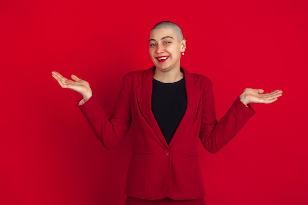 Sorridente, incerto. Ritratto di giovane donna calva caucasica isolata sulla parete rossa dello studio.