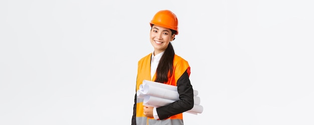 Sorridente ingegnere edile architetto femminile asiatico di successo in casco di sicurezza porta progetti e