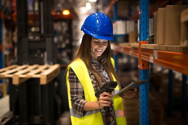 Sorridente lavoratore di sesso femminile che tiene tablet e scanner di codici a barre controllo inventario nel magazzino di distribuzione