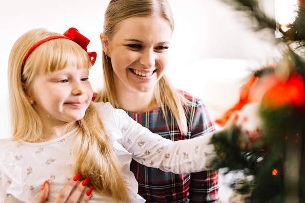 Sorridente madre e figlia che decorano albero di natale