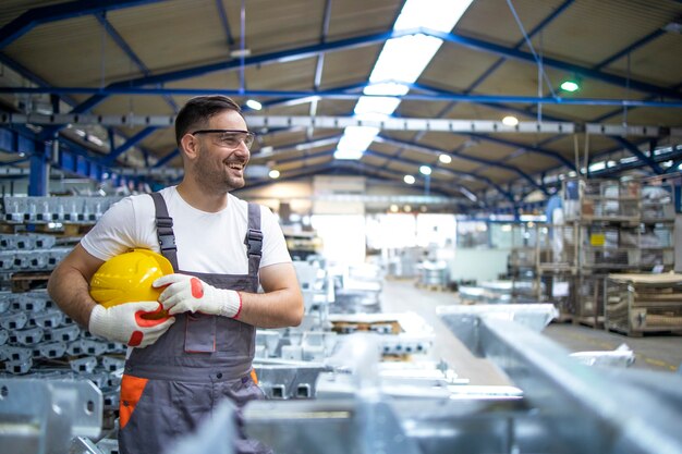 Sorridente operaio di fabbrica con elmetto in piedi nella linea di produzione in fabbrica