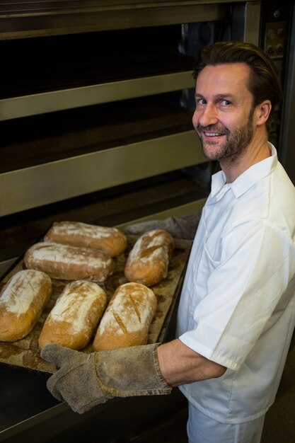 Sorridente panettiere portando un vassoio di panini cotti