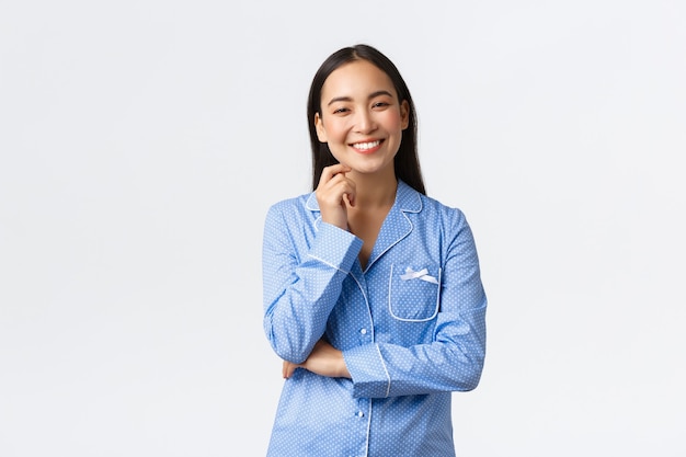 Sorridente ragazza asiatica felice in piedi in pigiama e guardando la fotocamera ottimista. Una studentessa organizza una divertente notte di pigiama party con le amiche, divertendosi. Ragazza che si diverte al pigiama party