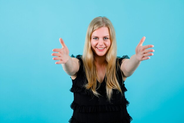 Sorridente ragazza bionda sta estendendo ahnds alla fotocamera su sfondo blu