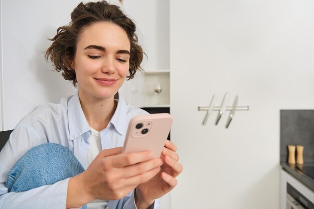 Sorridente ragazza bruna seduta con lo smartphone a casa ordina da asporto dall'app del telefono cellulare utilizzando on