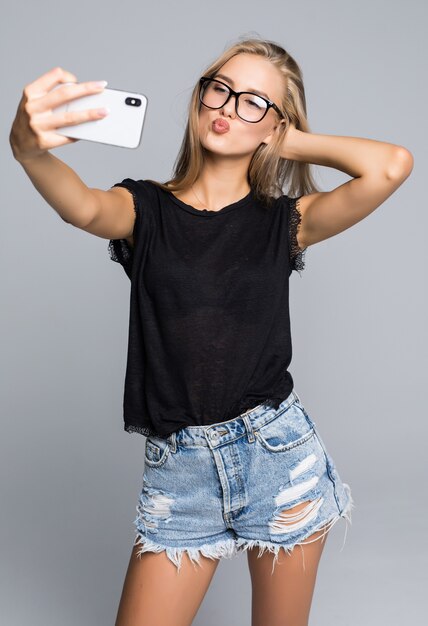 Sorridente ragazza giovane rendendo selfie foto sullo smartphone su uno sfondo grigio
