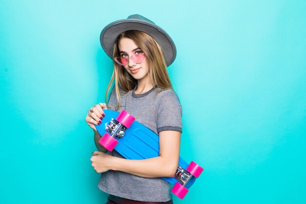 Sorridente skategirl adolescente sta con skateboard colorato isolato su sfondo verde