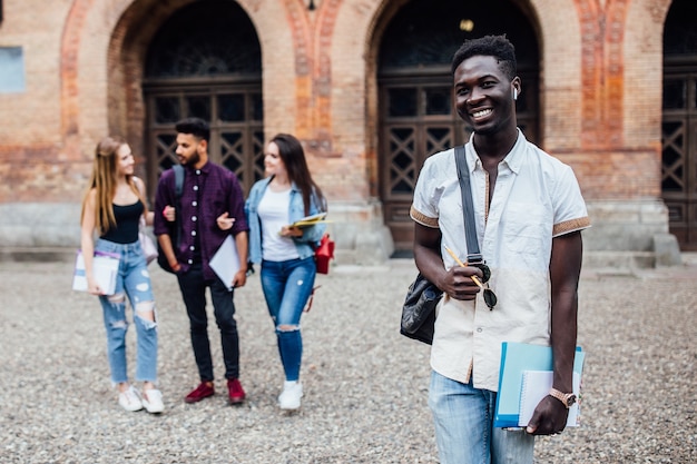 Sorridente studente nerd africano allegro di successo in piedi con i libri