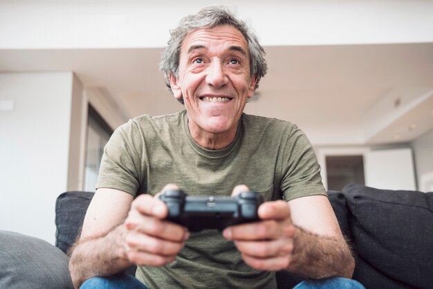 Sorridente uomo anziano seduto sul divano godendo la riproduzione del videogioco